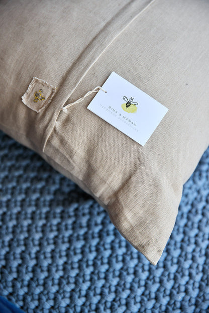 Back of a beige square pillow showing the 'bina x maman' label.