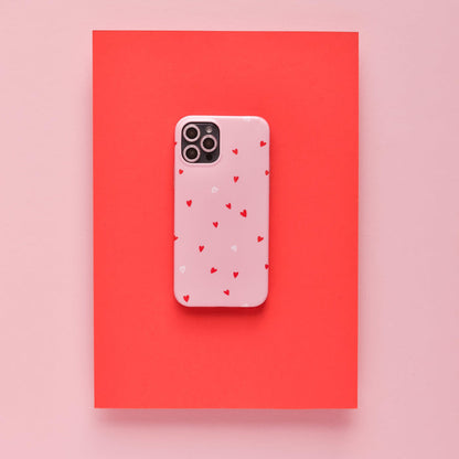 Pink glitter camera lens cover with pink phone case and red hearts on a red rectangle background.
