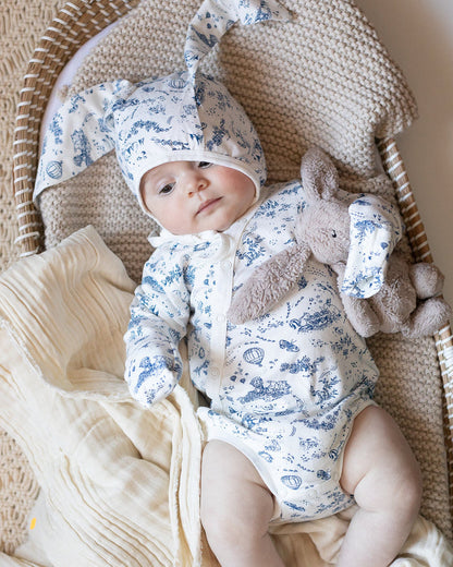Baby wearing a blue and white toile bonnet with bunny ears, and a blue and white toile bodysuit.
