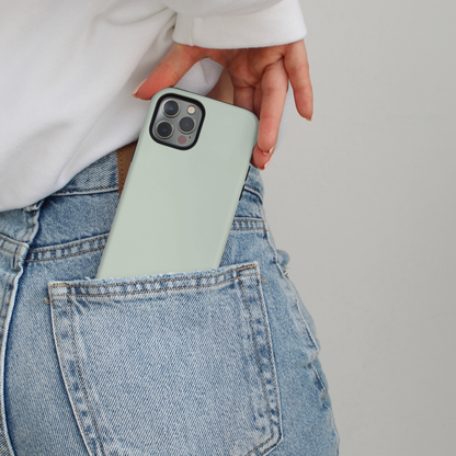 Person in jeans slips a sage green Coconut Lane Tough MagSafe phone case into their pocket, wearing a white top.